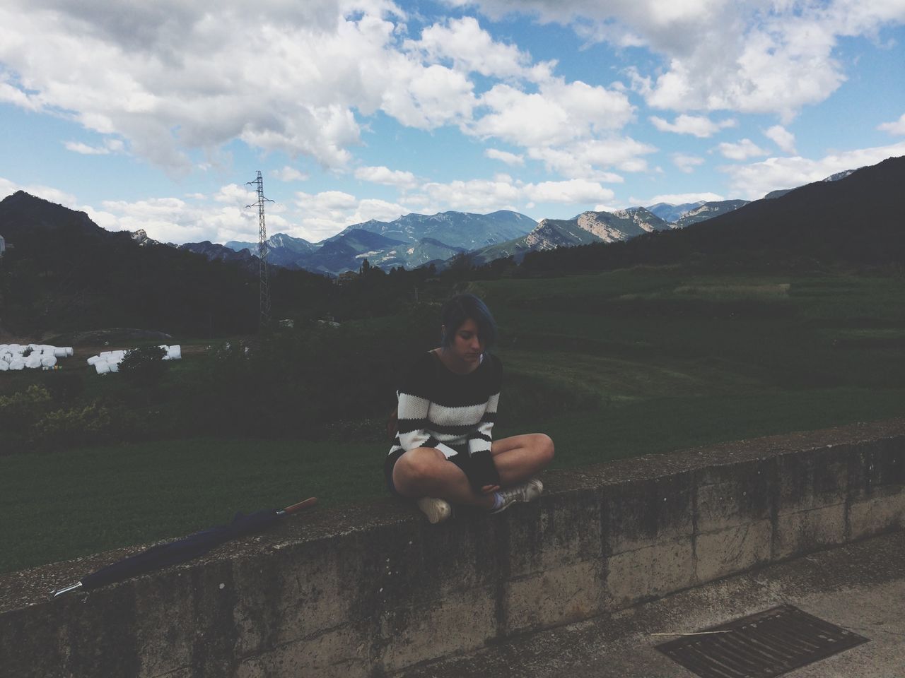 mountain, sky, lifestyles, leisure activity, mountain range, full length, cloud - sky, landscape, casual clothing, tree, sitting, young adult, cloud, nature, rear view, day, grass, outdoors