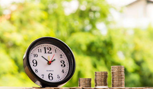 Close-up of coins stacked by alarm clock on table