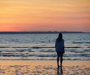 Rear view of woman standing on beach against sky during sunset