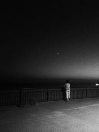 Man standing on railing against clear sky at night