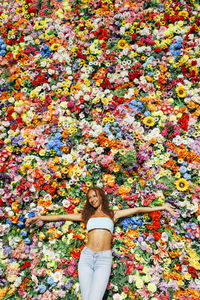 Smiling woman with arms outstretched standing in front of multi colored flower wall