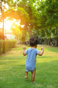 Rear view of baby boy walking on grassy field at public park