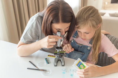 Woman looking through microscope sitting by daughter at home