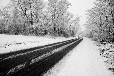 Empty road amidst snow covered bare trees