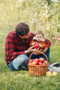 Father with baby boy holding apples on grassy land