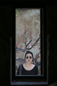 Portrait of young woman seen through window standing against wall