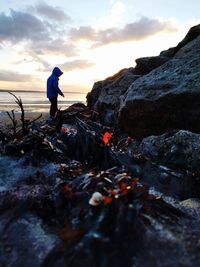 Man standing on rock against sky during sunset