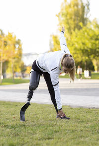 Focused paralympic female runner with leg prosthesis stretching body and doing forward bend during training