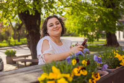 Portrait of young woman using mobile phone while sitting in park