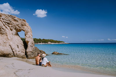 Woman sitting on shore at beach against sky