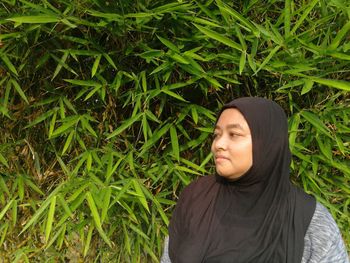 Thoughtful woman wearing hijab while standing against leaves