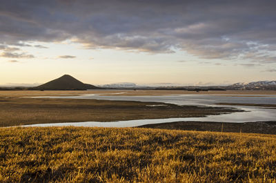 View from a grassy hill towards lake myvatn, partly covered with ice, and mount vindbelgjarfjall