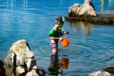 Boy holding bucket while standing river