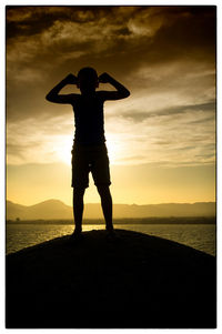 Rear view of silhouette man standing by sea against sky during sunset