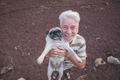 High angle portrait of smiling senior man carrying pug