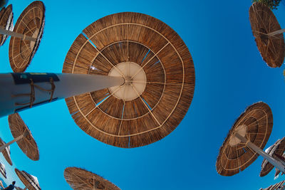 Low angle view of thatched roof parasols against clear blue sky
