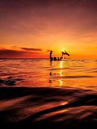 Silhouette people on sea against sky during sunset