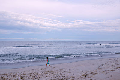 Full length of girl chasing seagull on beach against sky