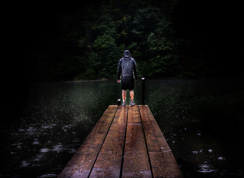 Rear view of man standing on pier over lake in forest