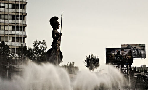 Low angle view of statue amidst fountain against sky in city