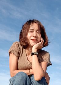 Portrait of young woman sitting against sky