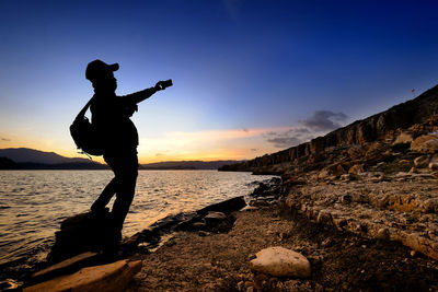 Silhouette man photographing while standing at beach during sunset