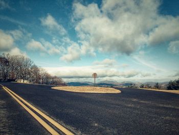 Empty road by trees against sky