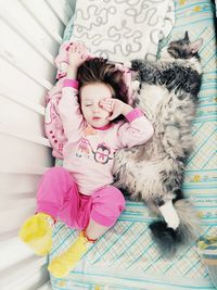 High angle view of cute girl lying with cat in crib at home