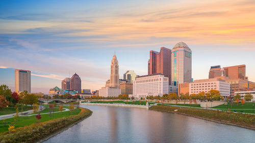 River amidst buildings against sky during sunset