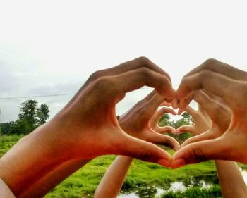 Close-up of heart shape with hand on tree against sky