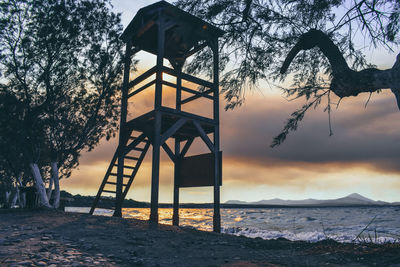 Lifeguard hut on beach against sky during sunset