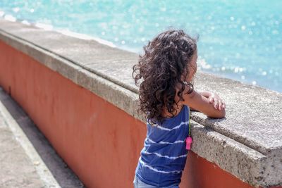 Side view of girl looking at sea while standing by retaining wall