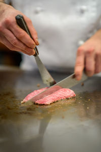 Close-up of chef's hand cutting and preparing steak