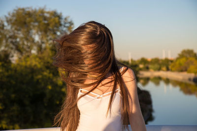 Young woman with tousled hair standing by railing over river