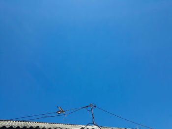 Low angle view of electricity pylon against clear blue sky