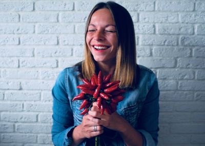 Smiling young woman holding red while standing against brick wall