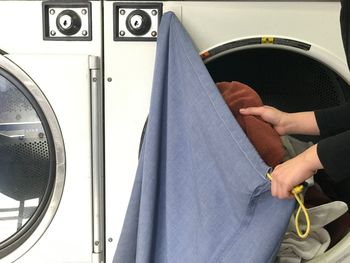 Midsection of woman putting clothes in washing machine