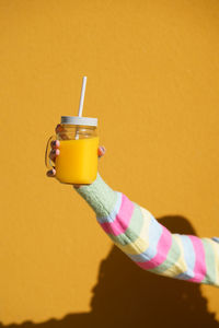 Close-up of hand holding coffee cup against yellow background