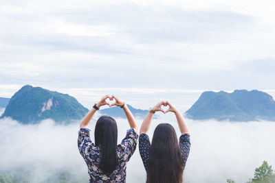 Rear view of women making heart shape while looking at mountains