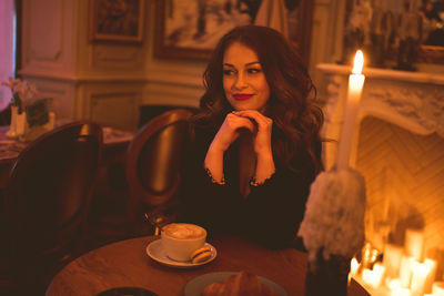 Smiling woman sittin in cafe with latte coffee and burning candle on table closeup. cozy atmosphere