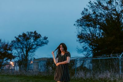 Beautiful woman standing against sky at dusk