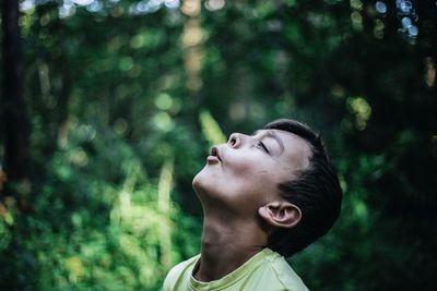 Close-up of boy blowing while standing against trees