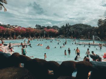 Crowd in swimming pool against cloudy sky