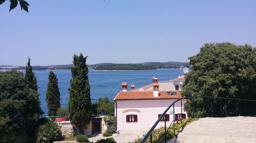 Houses and trees by sea against clear blue sky