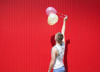 Man holding balloons while standing against red wall