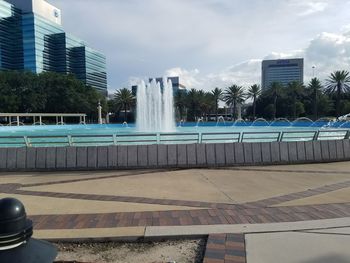 Fountain by swimming pool in city against sky