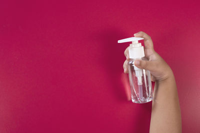 Close-up of hand holding glass bottle against red background