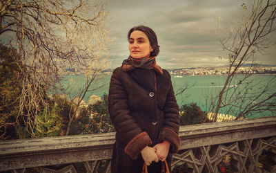 Portrait of young woman standing against bare trees in winter