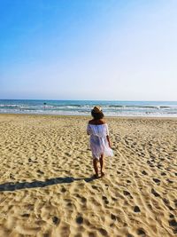 Woman with hat from behind looks at the sea