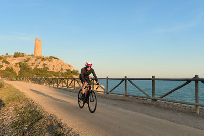 Coastal landscape and cyclist riding along a road at sunset.